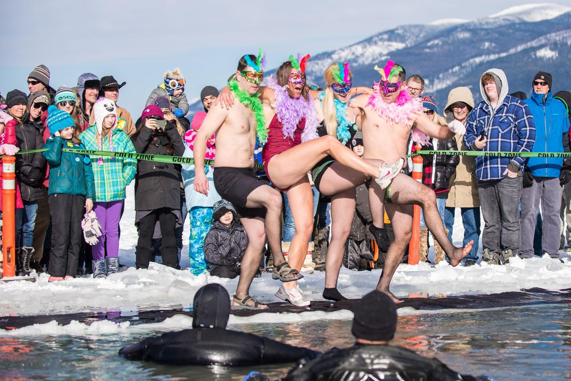 Whitefish Montana winter carnival attendees in bathing suit costumes plunging into polar water of a frozen lake.