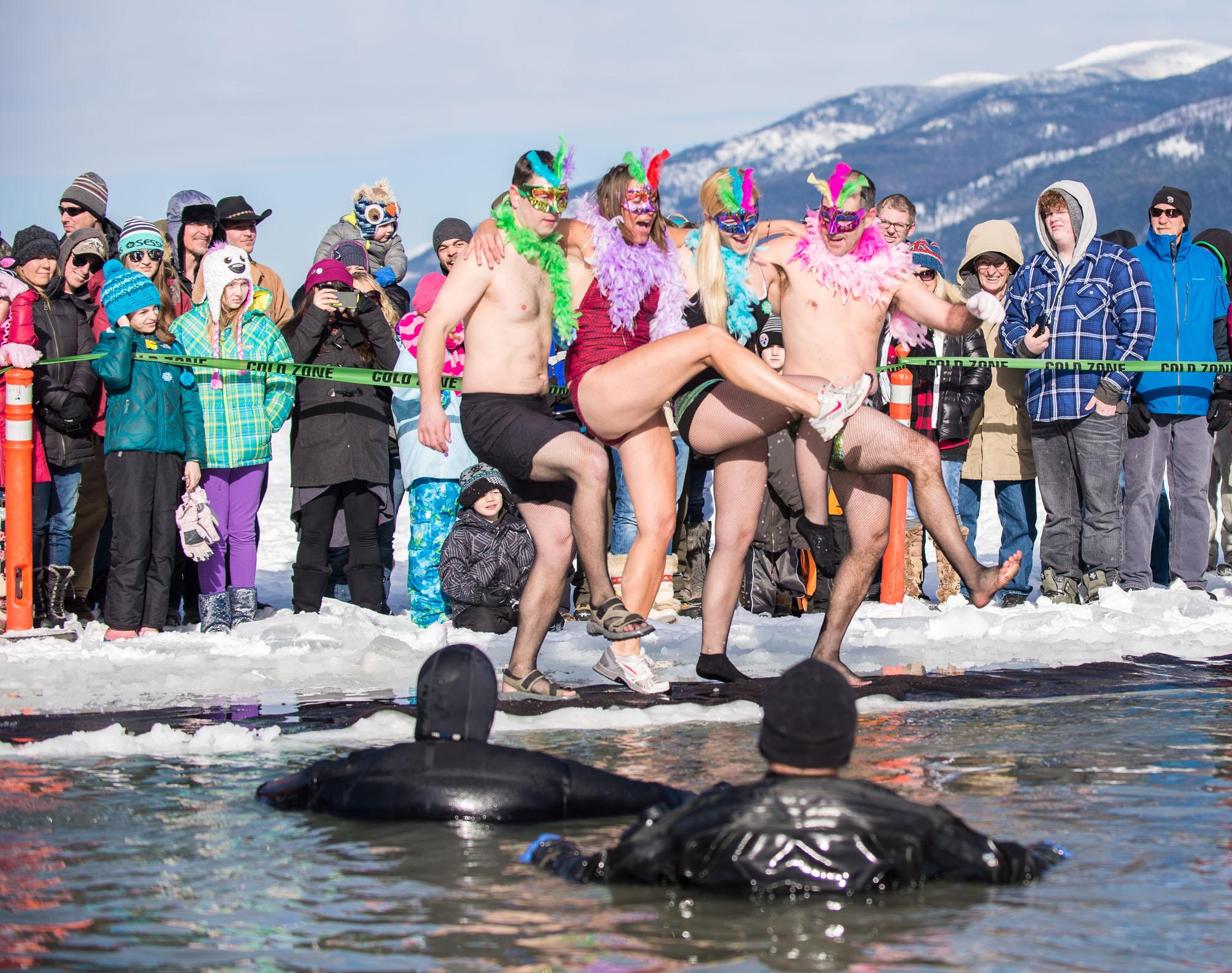 Whitefish Montana winter carnival attendees in bathing suit costumes plunging into polar water of a frozen lake.