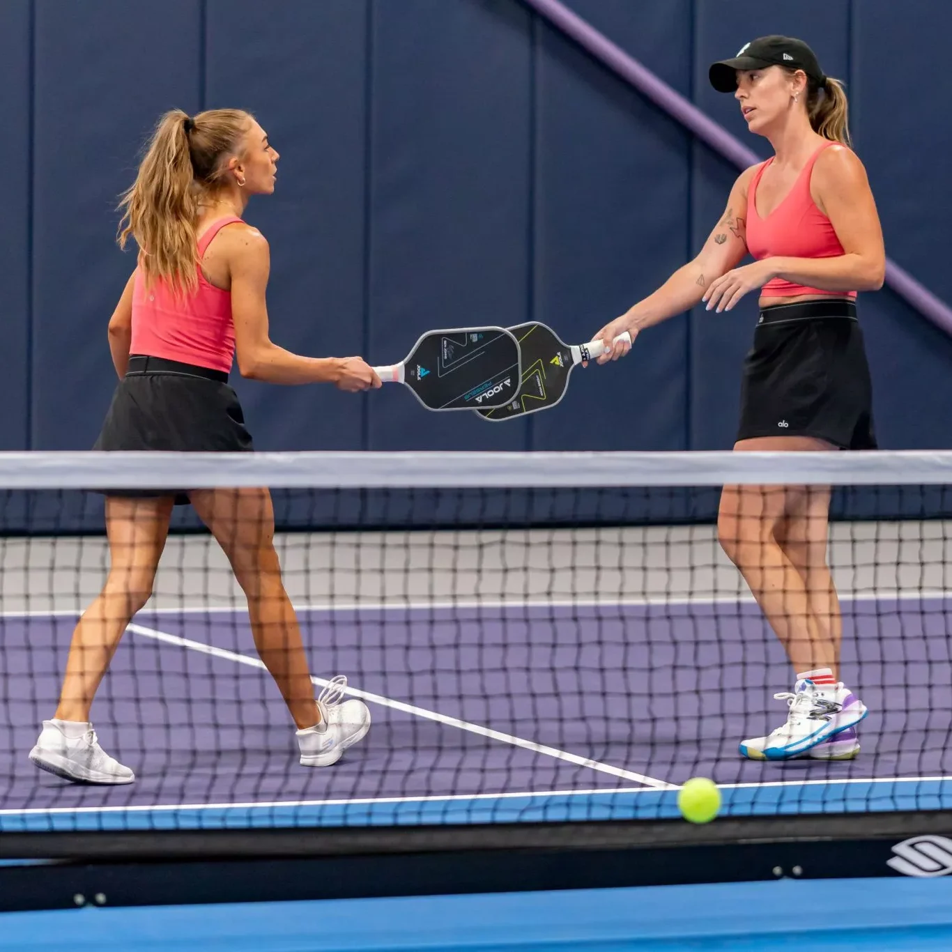 Women tapping their pickleball rackets in a mock “high five”